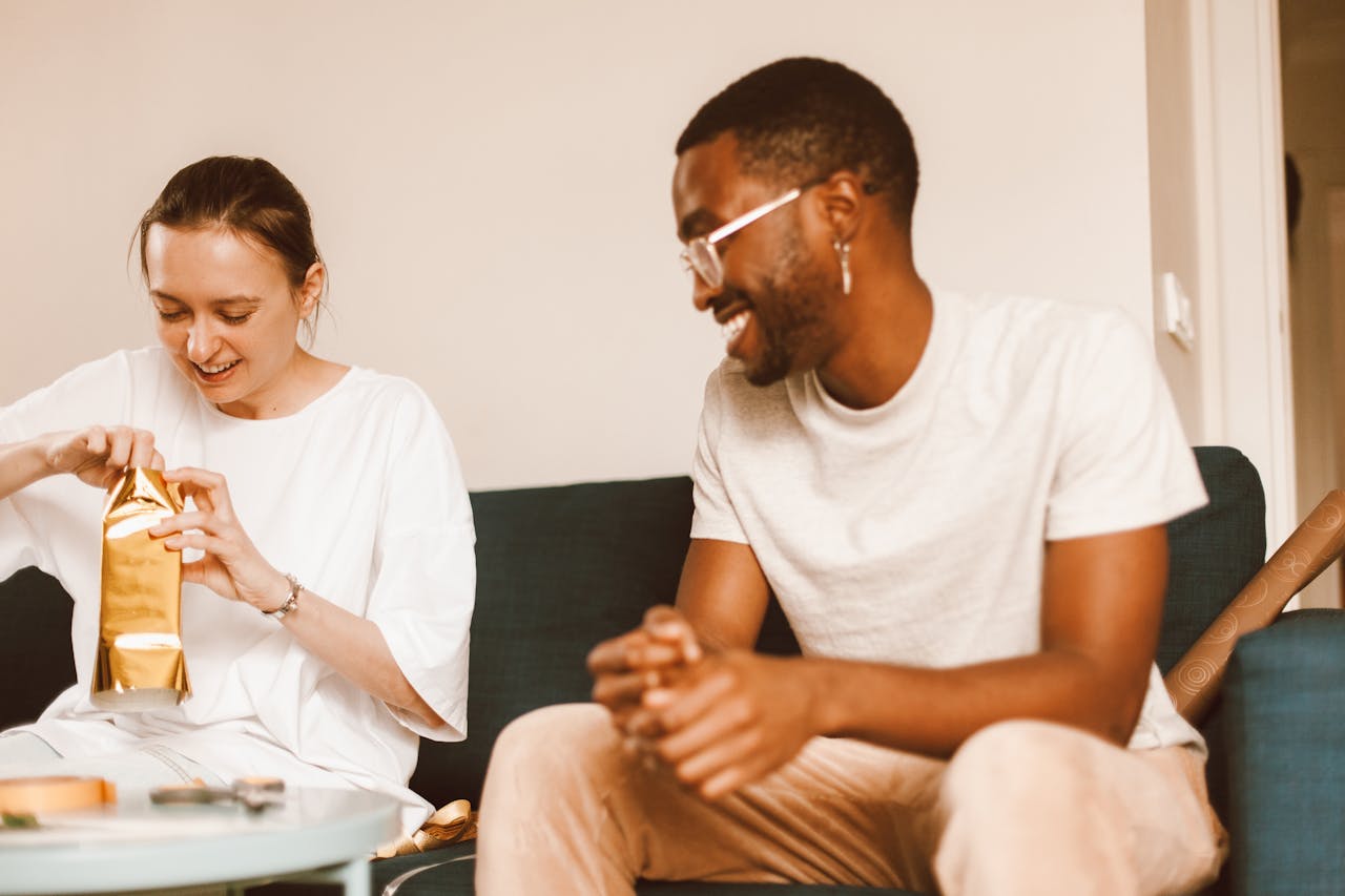 A happy interracial couple opening a gift while sitting together on a couch at home.